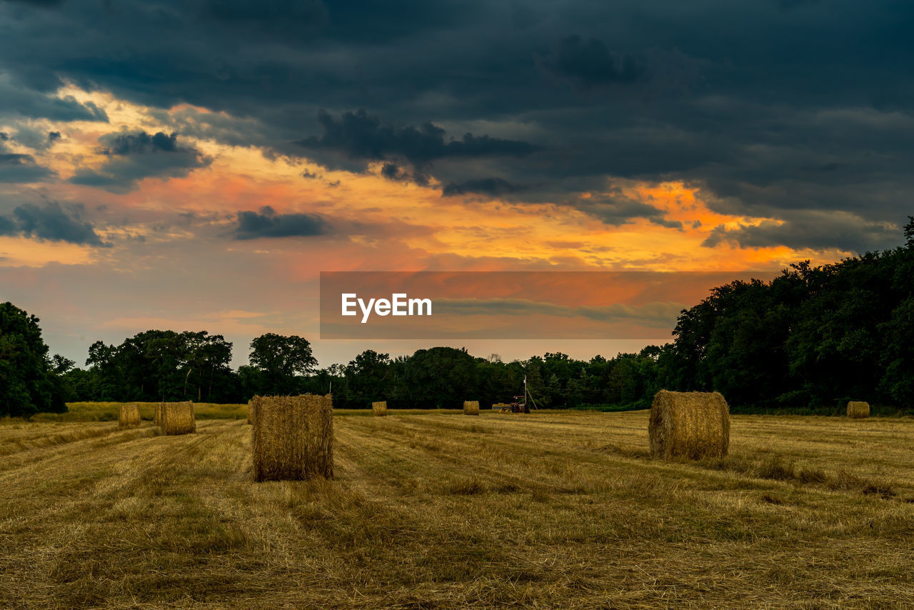 Hay bales on field against sky during sunset