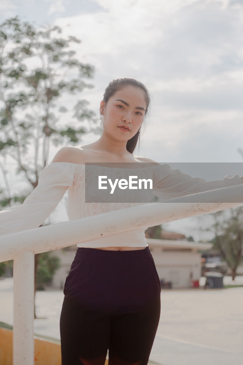 Portrait of young woman standing by railing