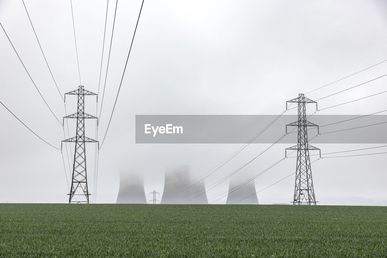 Uk, england, rugeley, electricity pylons standing in field during foggy weather with cooling towers in background