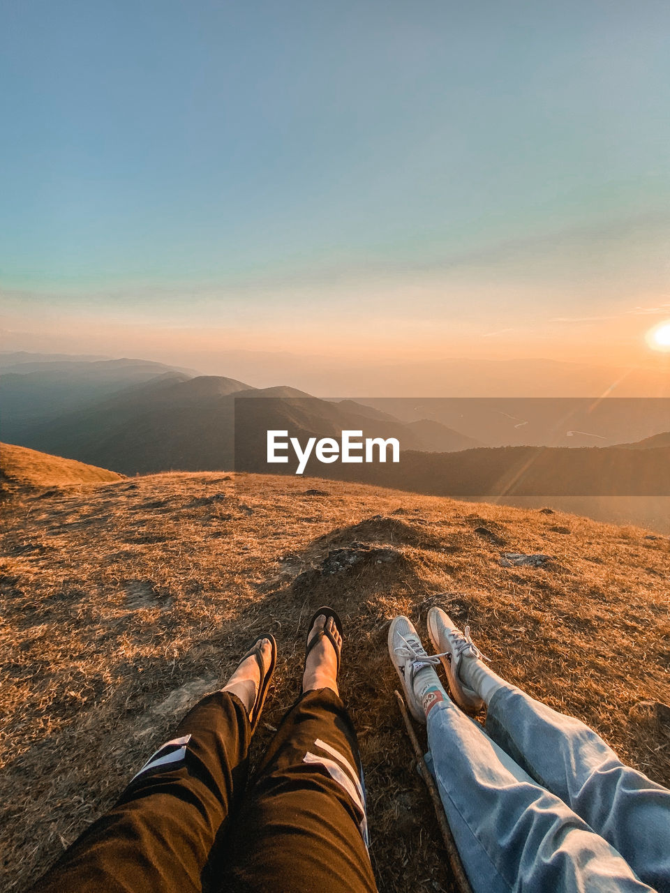 Low section of people sitting on mountain against sky during sunset
