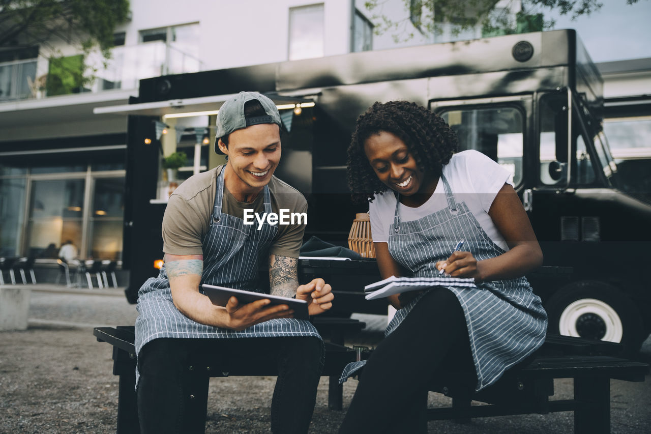 Smiling male and female owners working against food truck in city