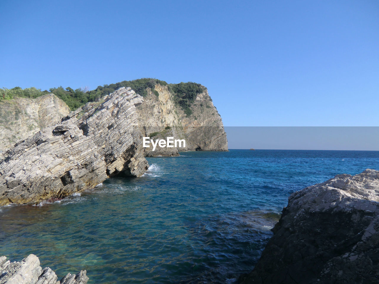 Rock formations by sea against clear blue sky