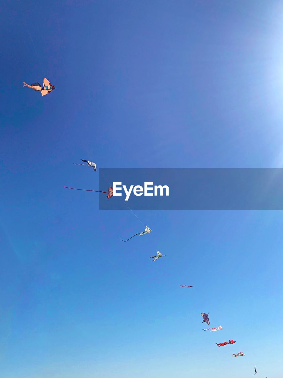 Low angle view of kites flying against clear blue sky