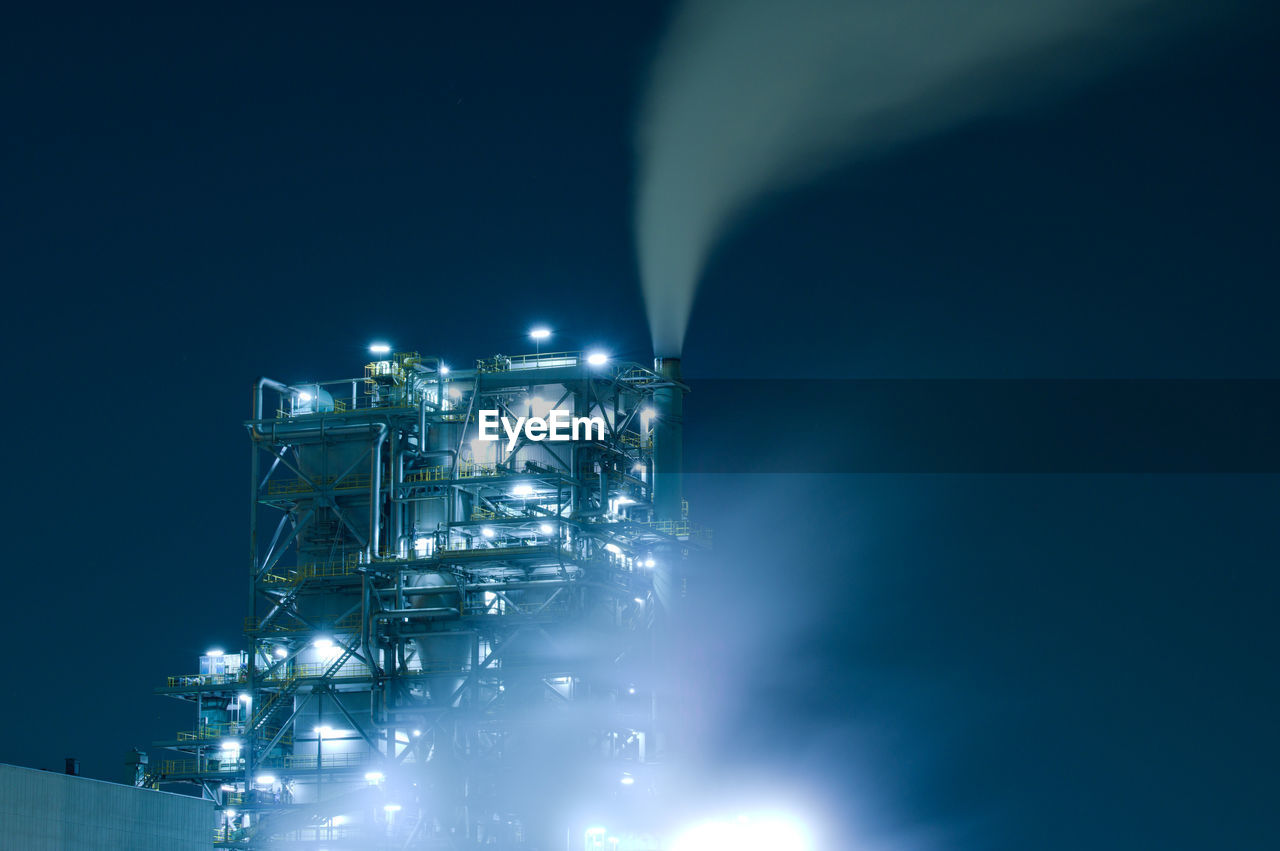 Low angle view of illuminated factory against sky at night