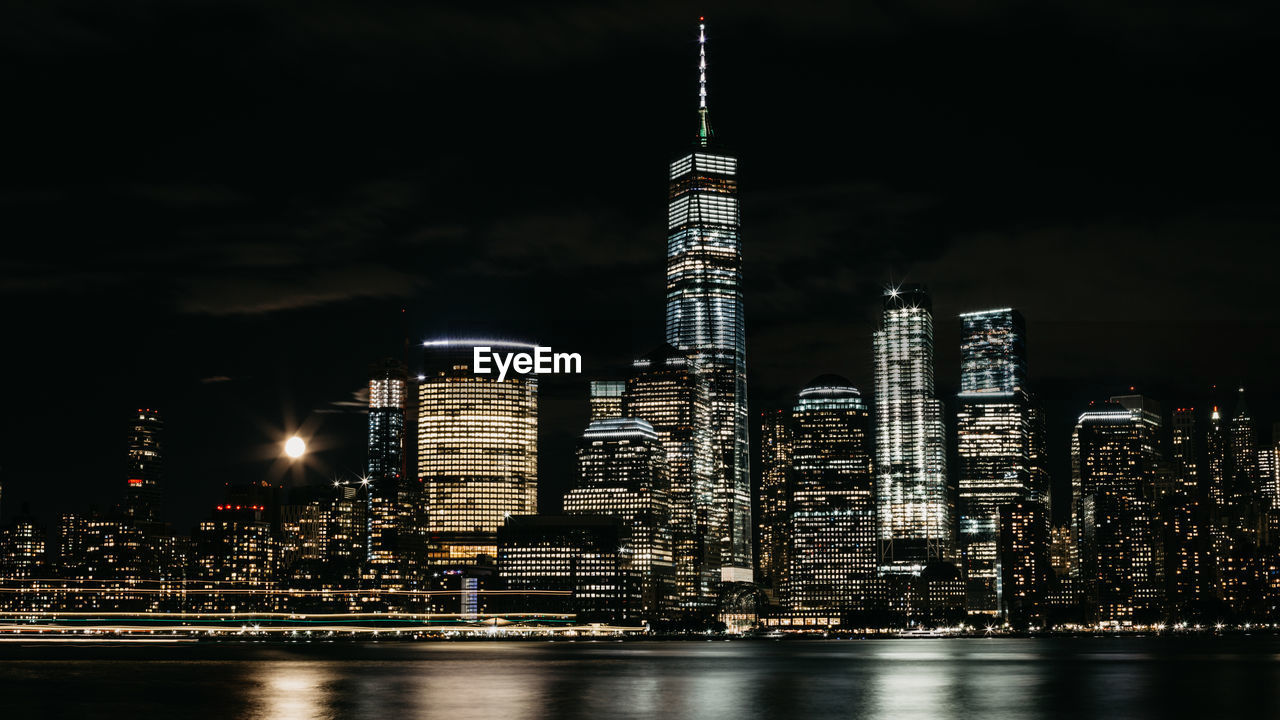 Illuminated buildings by river against sky in city at night