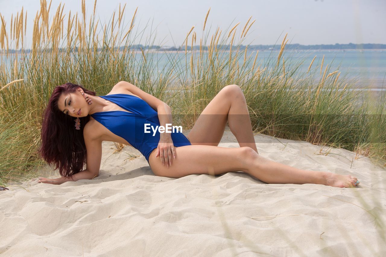 Sensuous young model wearing blue swimwear while lying at beach