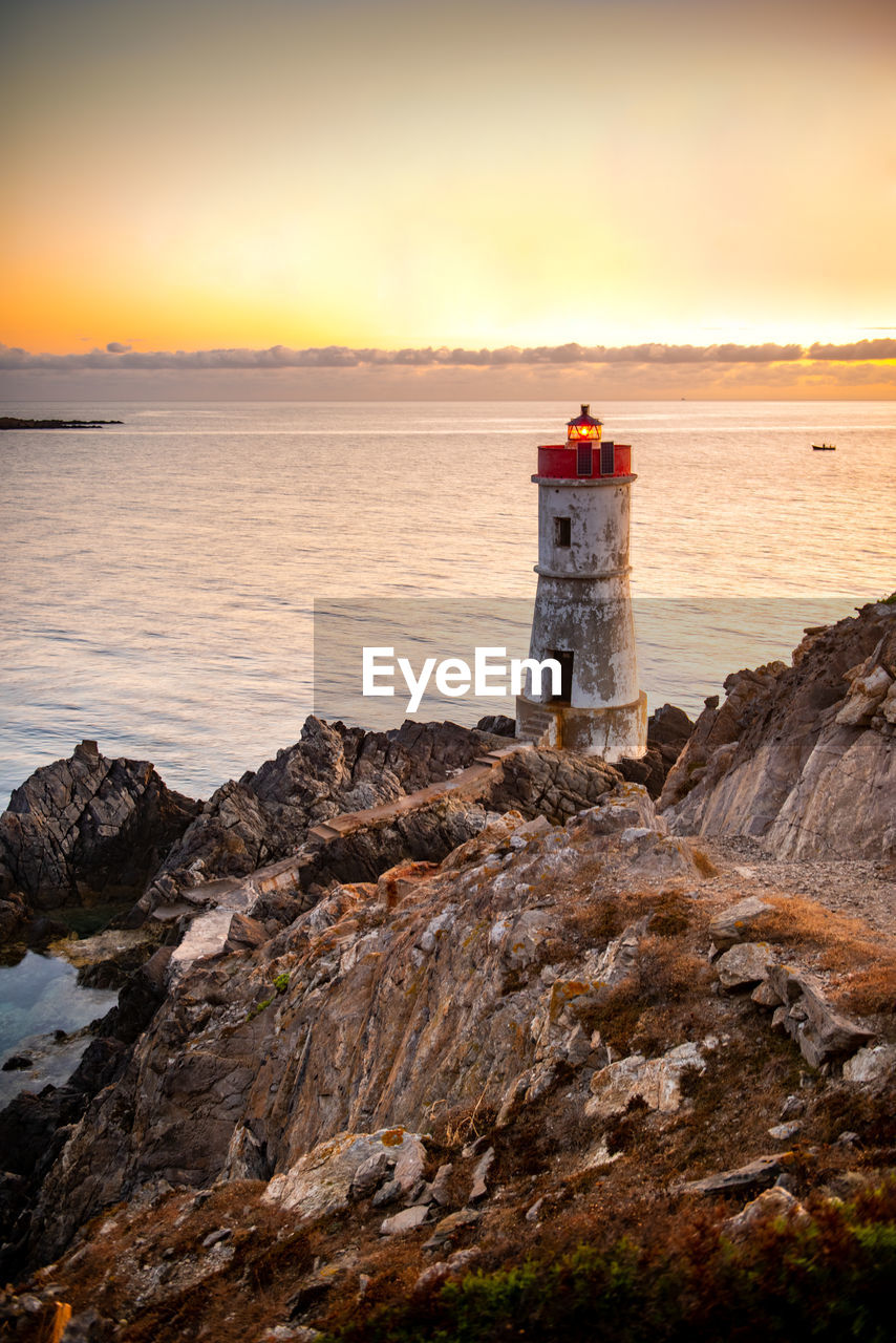 Lighthouse by sea against sky during sunset