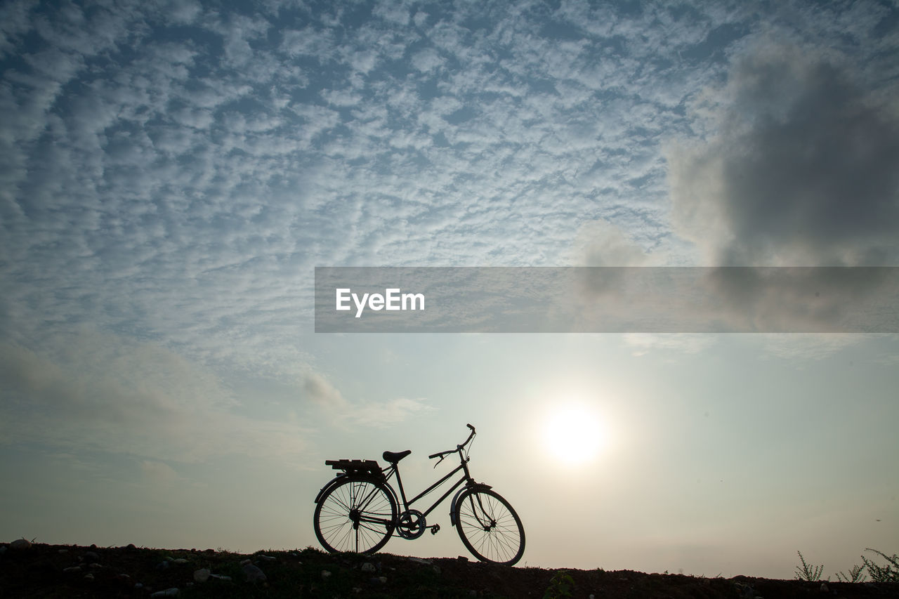 SILHOUETTE MAN RIDING BICYCLE ON FIELD AGAINST SKY