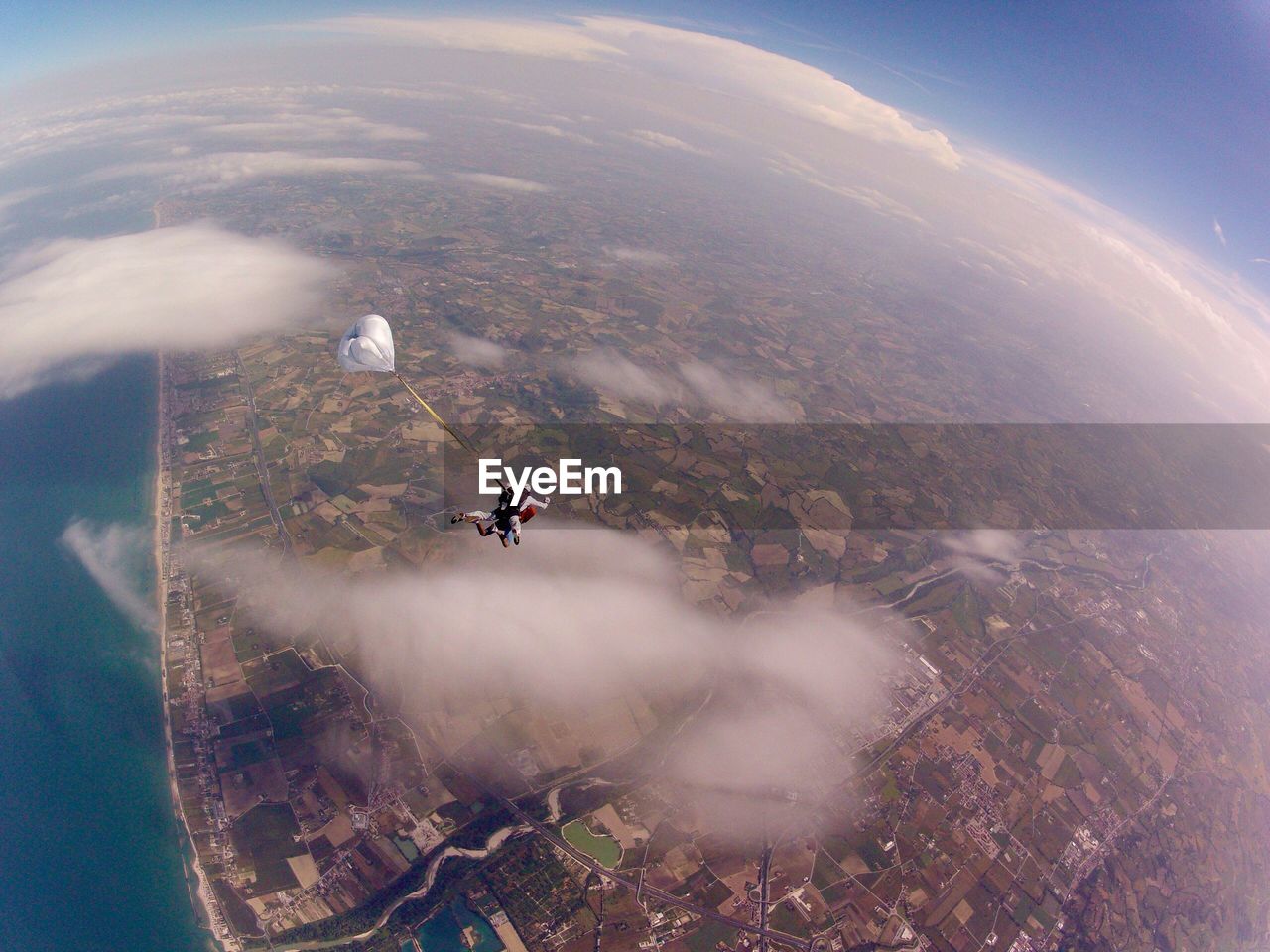 Aerial view of people paragliding over landscape by sea