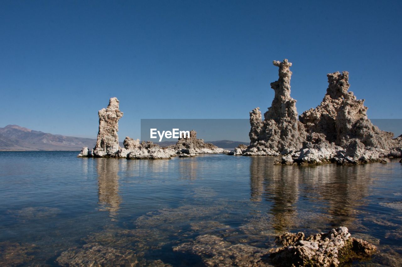 View of rock formation in sea against clear blue sky