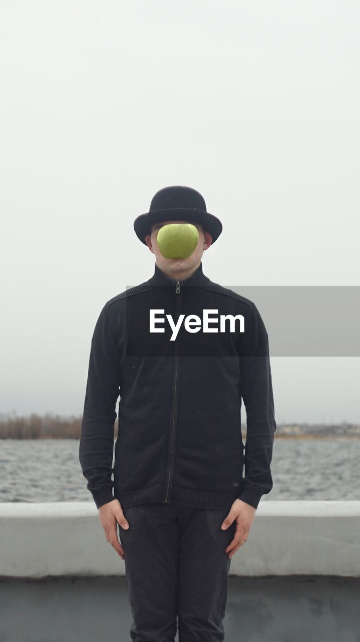 Man by water with apple in front of face