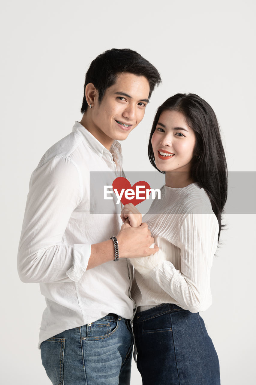 Portrait of young couple holding heart shape standing against white background