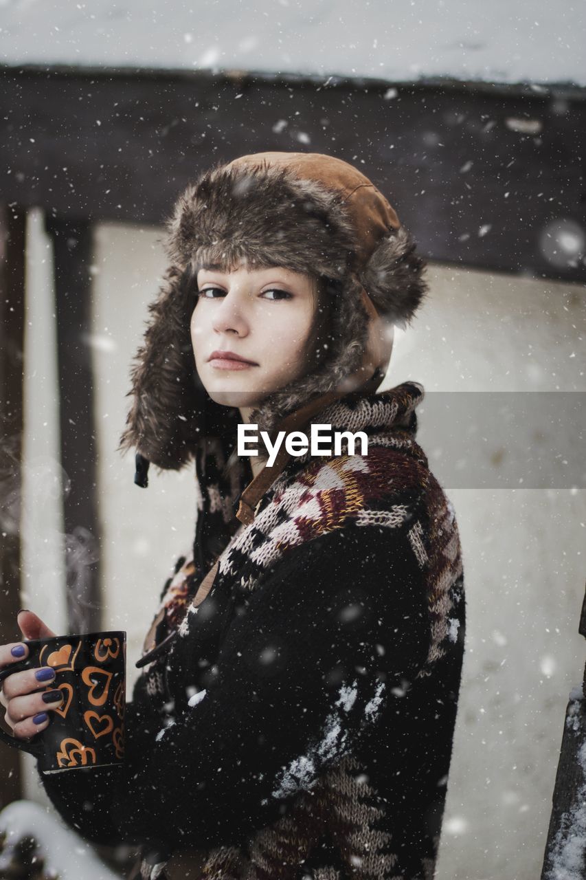 Portrait of woman holding a cup of coffee while it snows