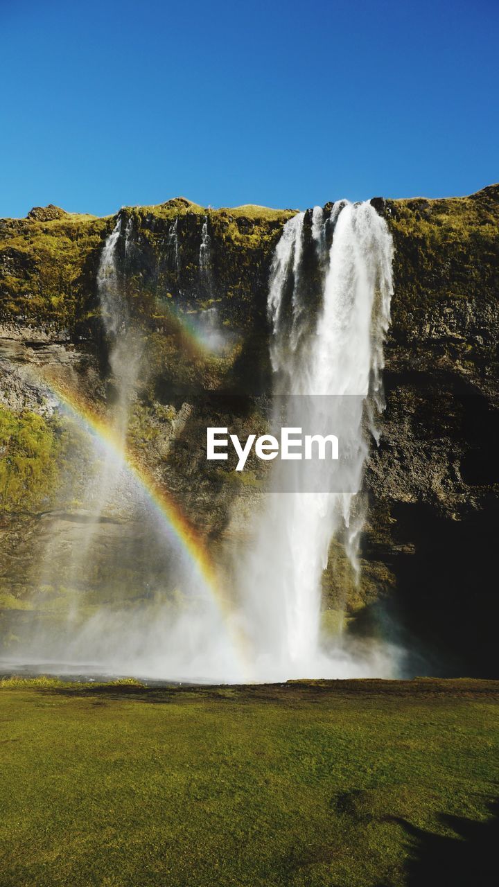 LOW ANGLE VIEW OF WATERFALL AGAINST RAINBOW IN SKY