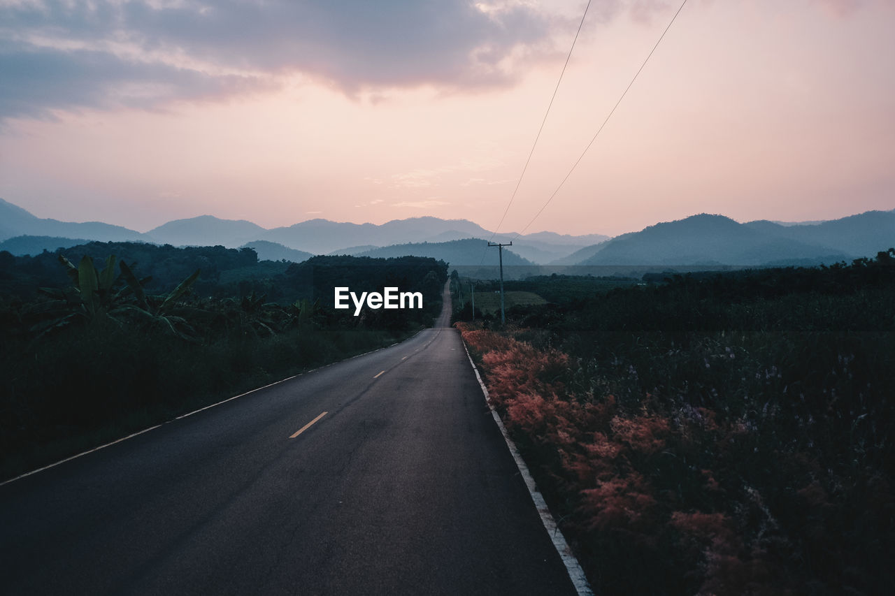 Road by mountains against sky during sunset