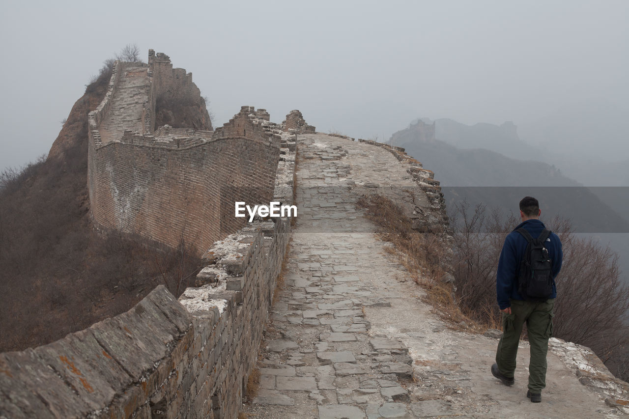 Rear view of man walking on great wall of china in foggy weather