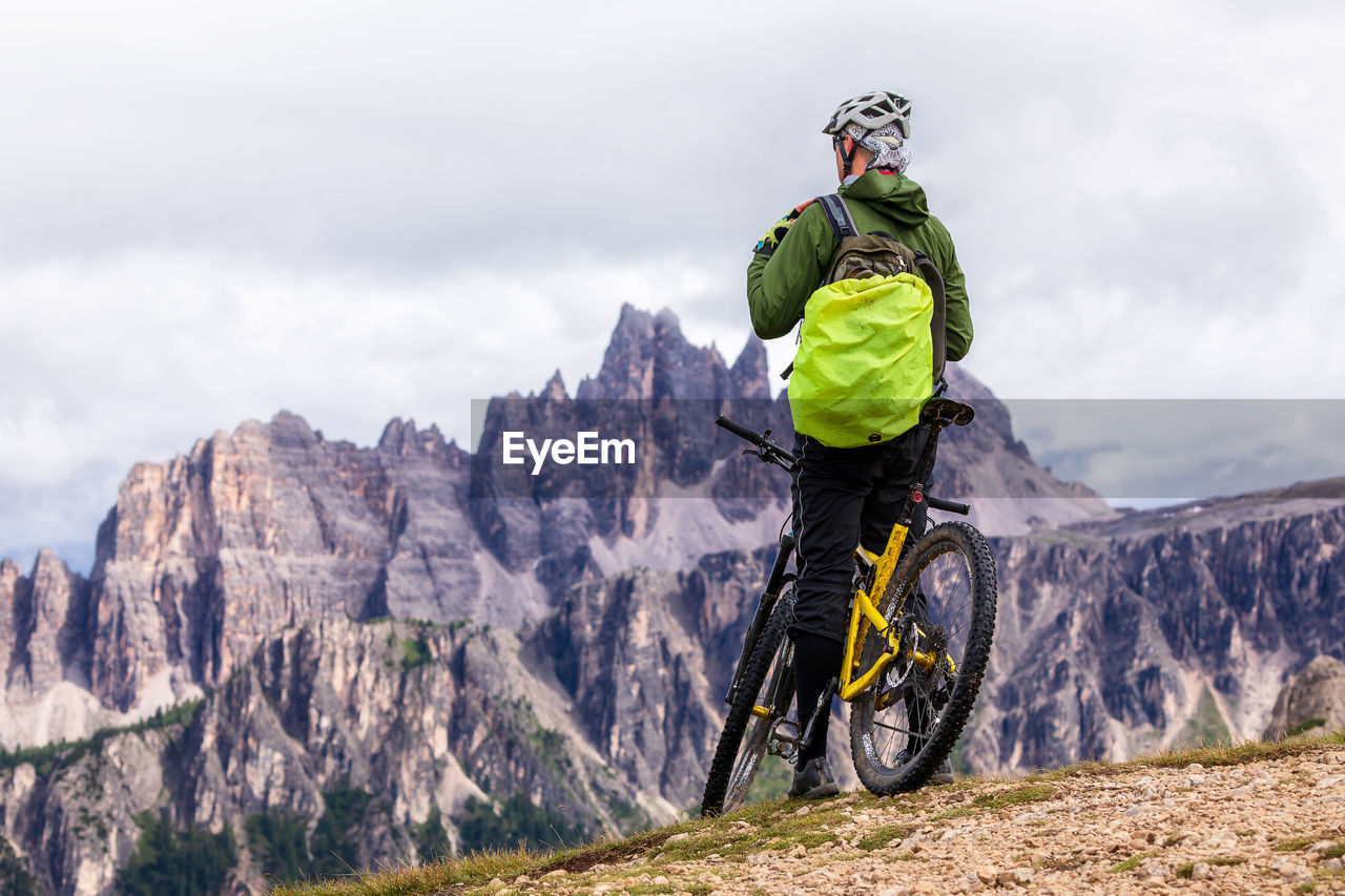 Rear view of person with bicycle on mountain against cloudy sky