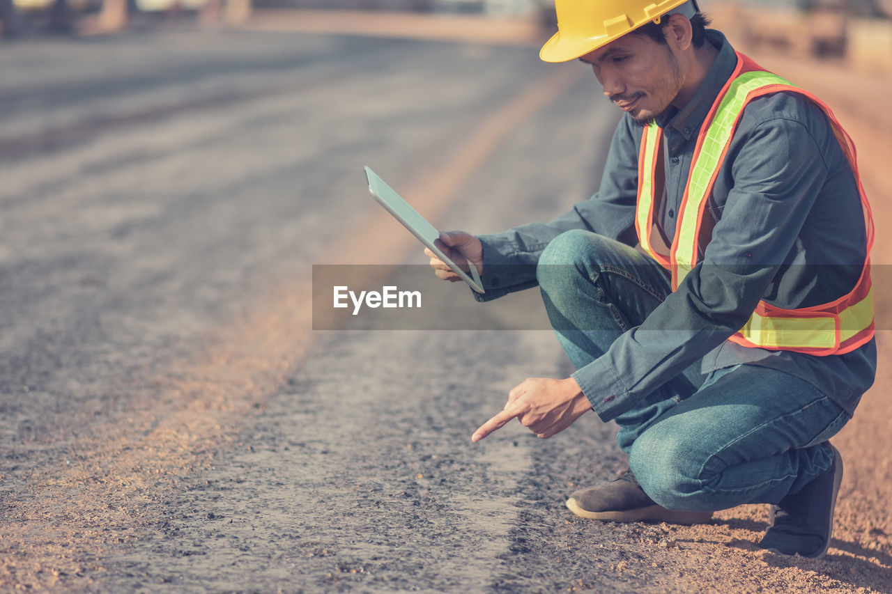 Side view of engineer using digital tablet while crouching on road