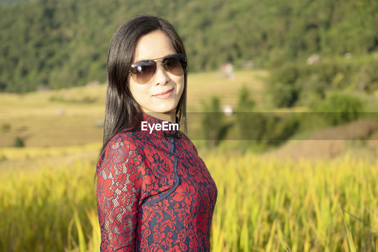 PORTRAIT OF YOUNG WOMAN STANDING ON FIELD