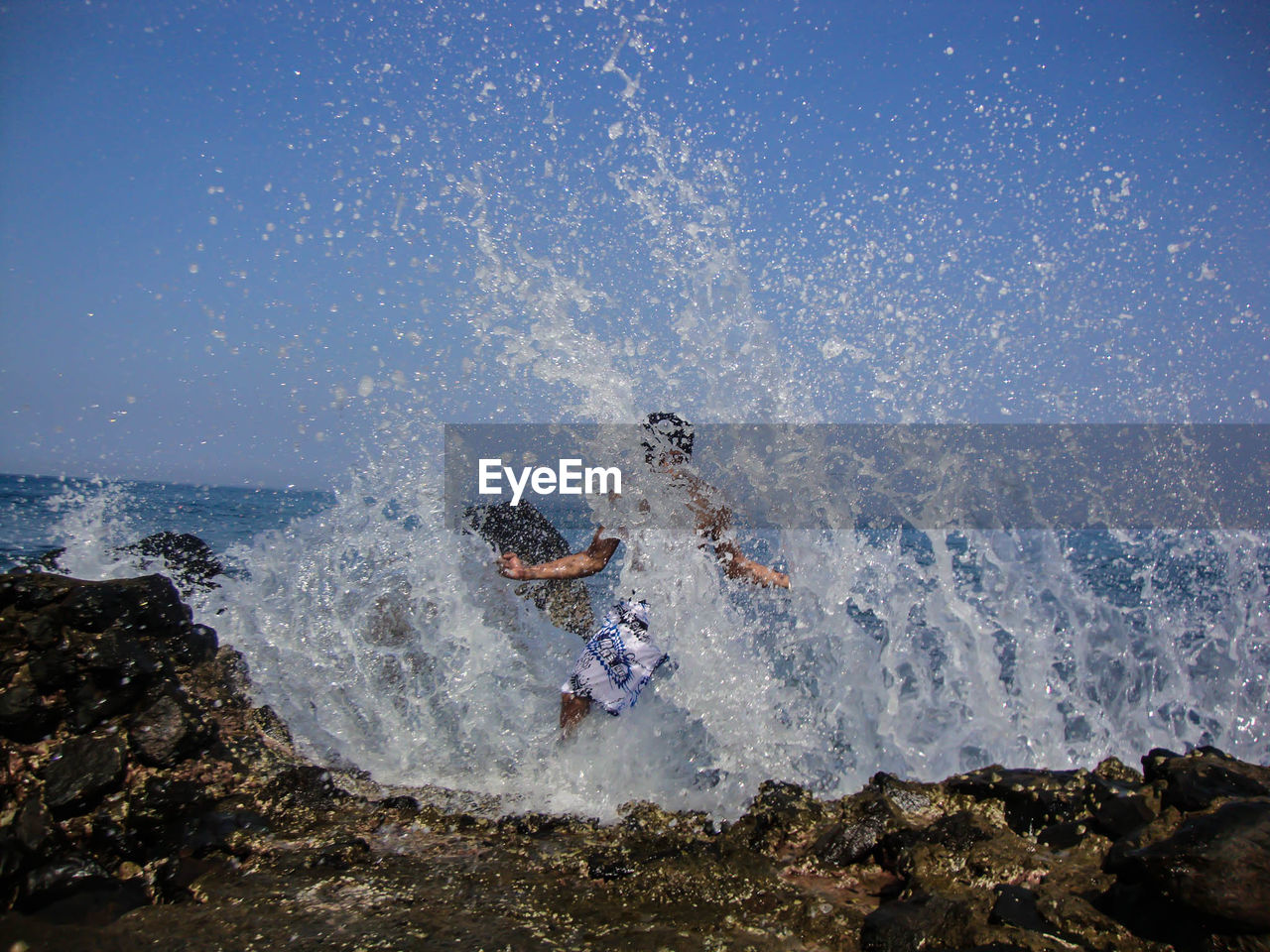 Waves splashing on man standing at beach against sky