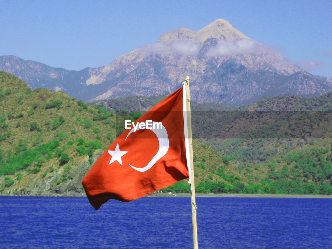 RED FLAG BY LAKE AGAINST MOUNTAIN RANGE