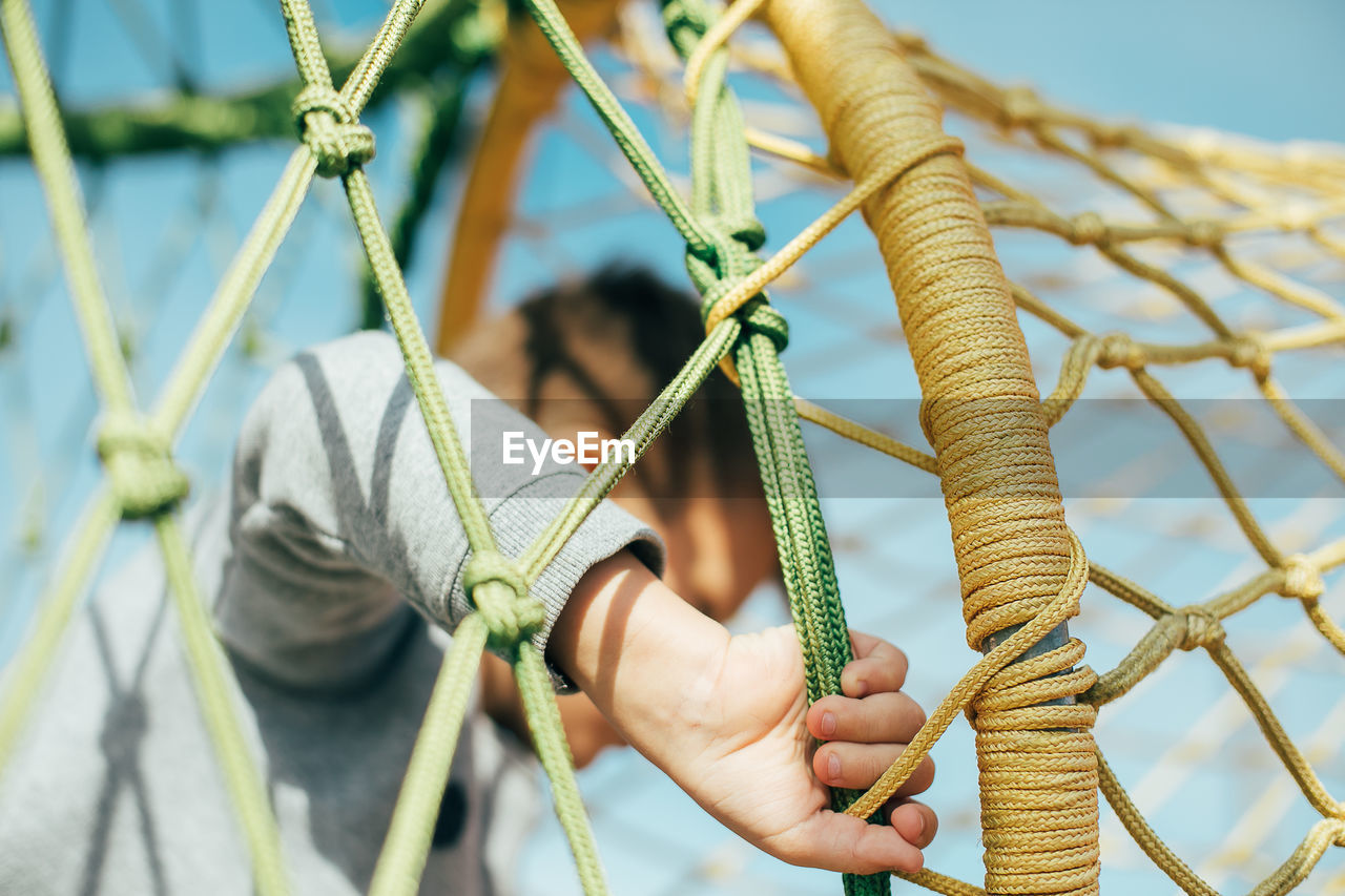 CLOSE-UP OF HAND HOLDING ROPE TIED TO ROPES