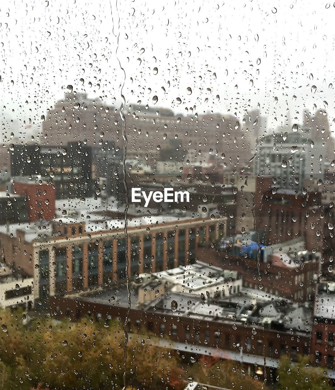 Buildings in city against sky seen through wet window during rainy season