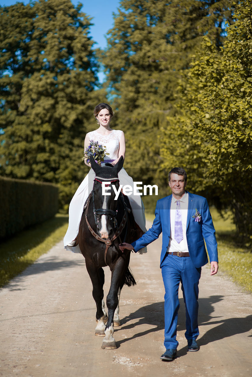 Portrait of bride and groom with horse walking on road