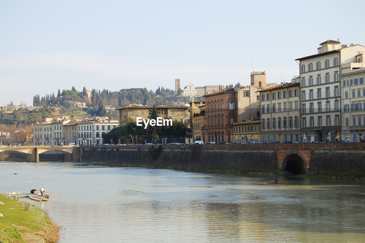 Bridge over river by buildings against clear sky