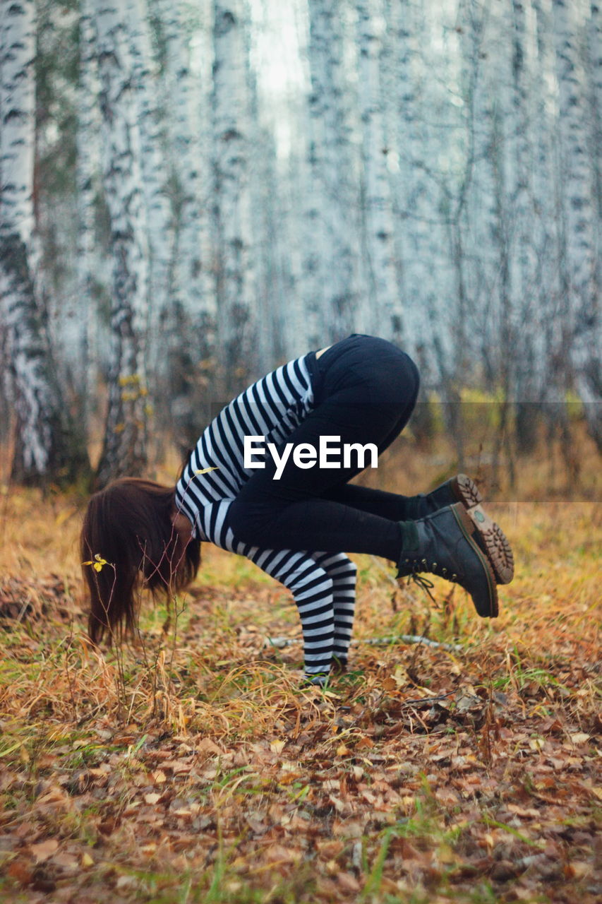 Side view of woman practicing handstand in forest