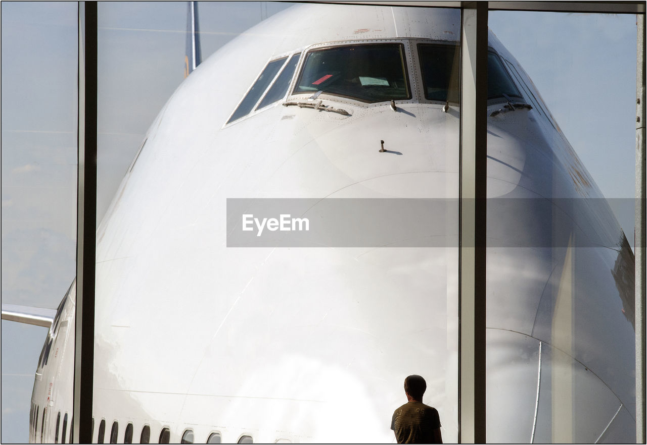 Rear view of man looking at airplane through window