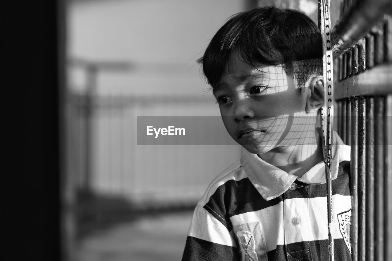 Close-up of boy looking away while standing by fence