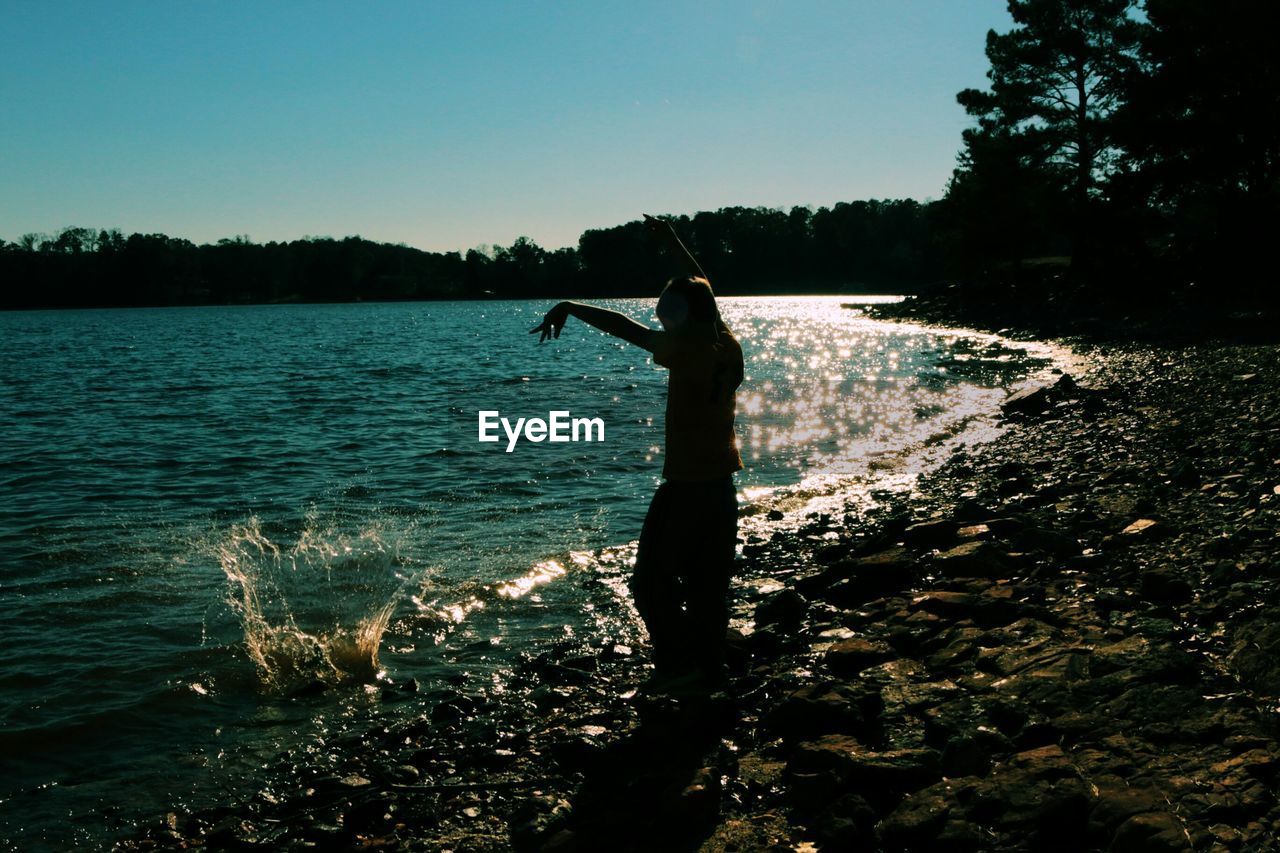 Girl throwing rocks in water at lakeshore