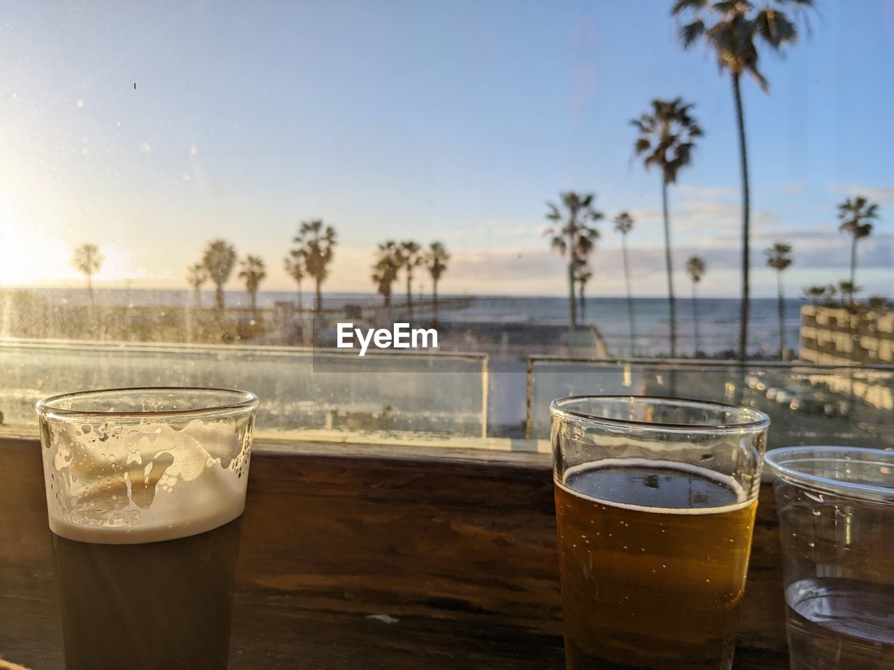 food and drink, drink, drinking glass, palm tree, glass, sky, refreshment, tropical climate, household equipment, water, nature, table, alcohol, no people, tree, morning, sunlight, beach, outdoors, day, land, sea, food, focus on foreground, plant, travel destinations, soft drink, restaurant, chair