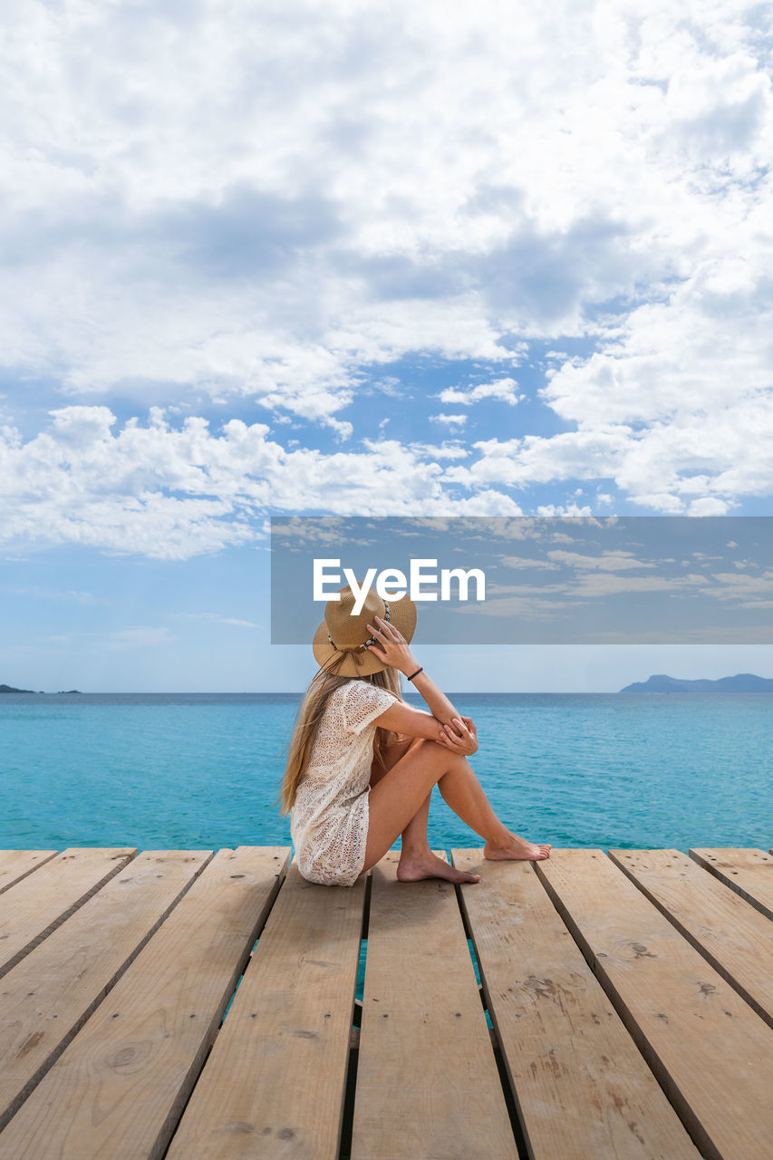 rear view of woman sitting on pier at beach against sky