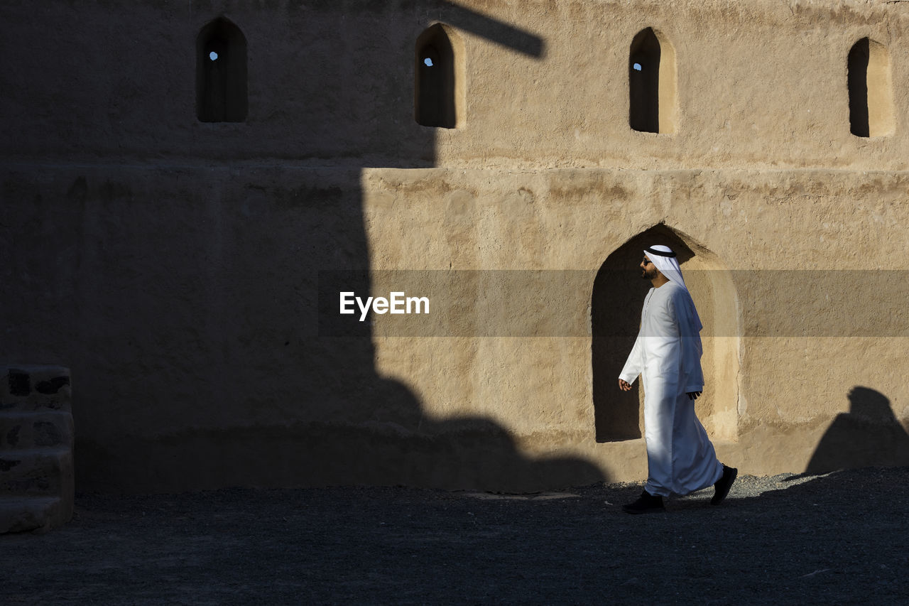 Side view of man wearing traditional clothing walking by old building