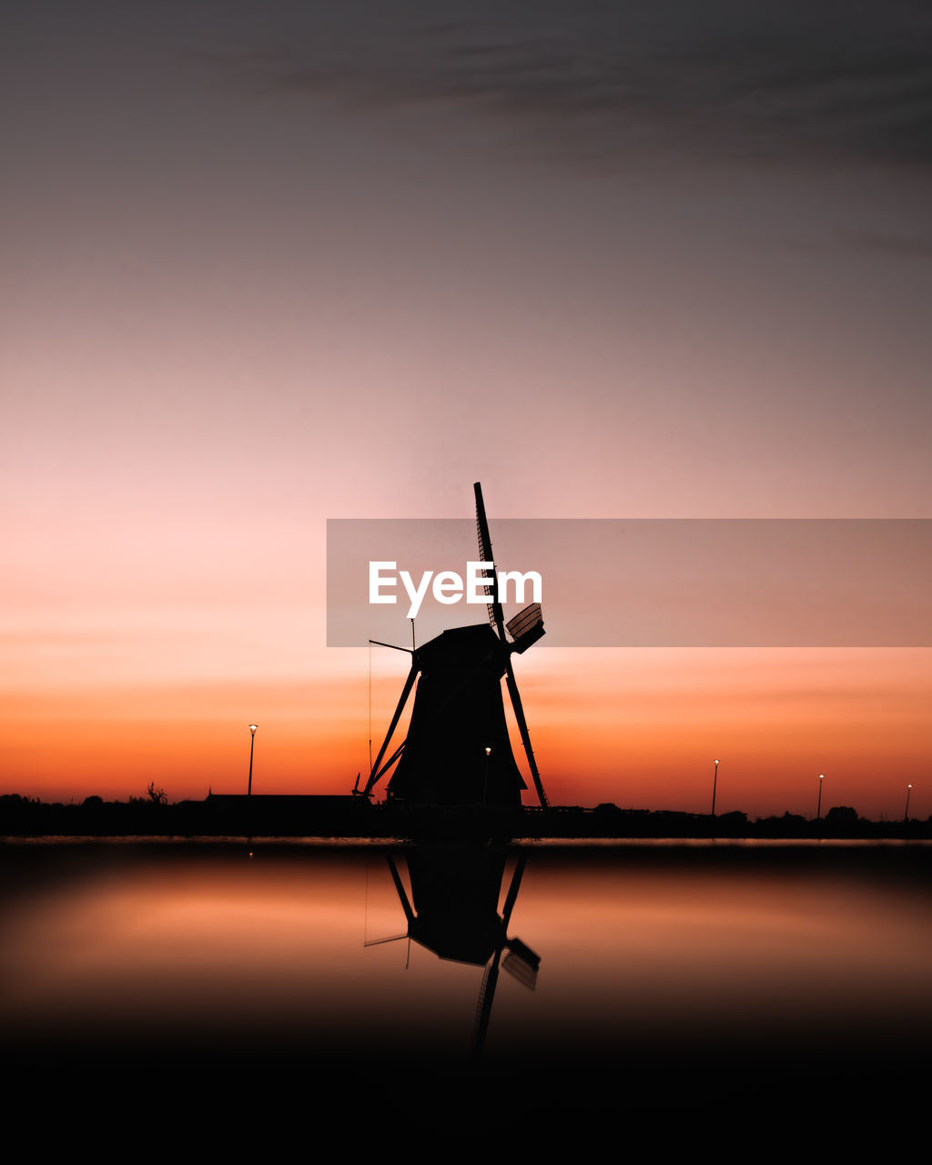 Silhouette of a mill against sky during sunset