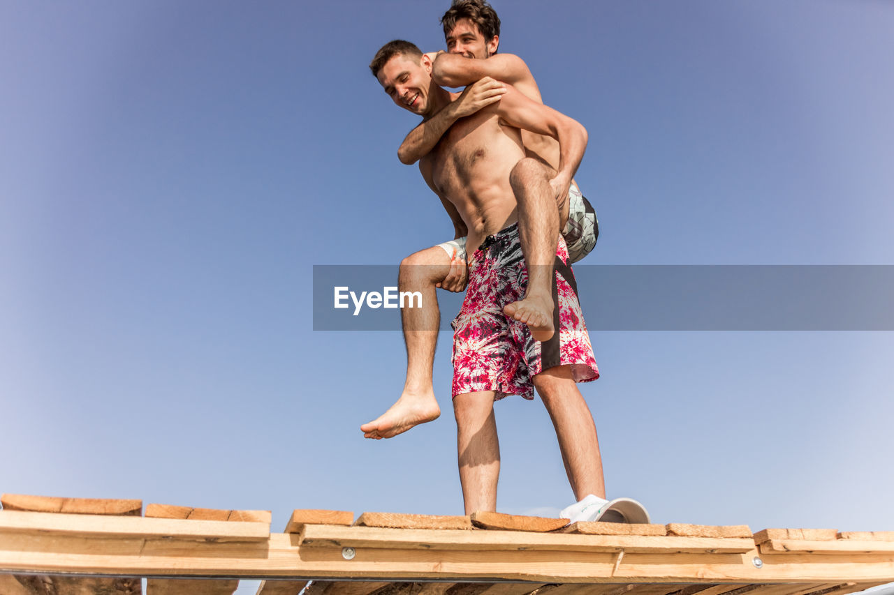 Low angle view of friends standing against clear blue sky