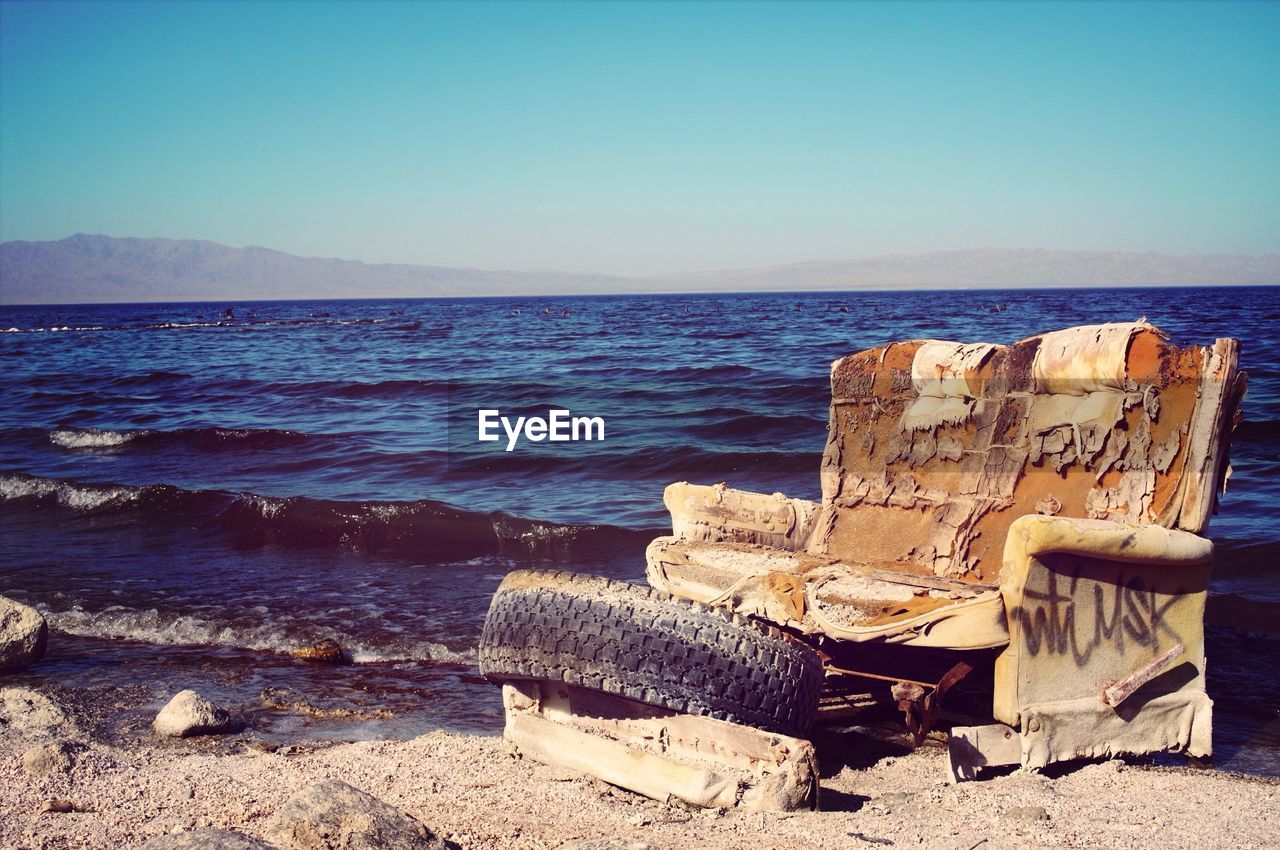 Obsolete sofa and tire at beach against clear blue sky