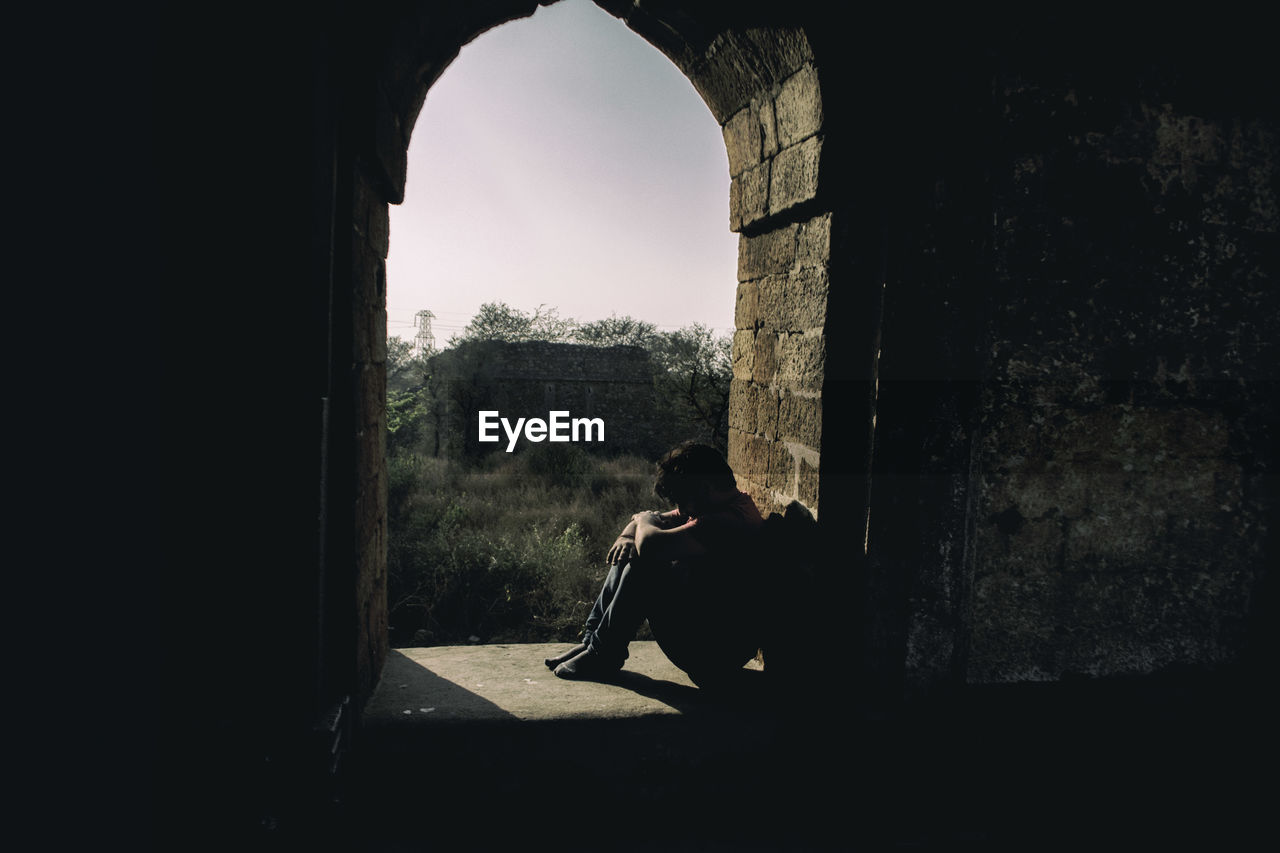 Depressed man sitting at arch window of historic building