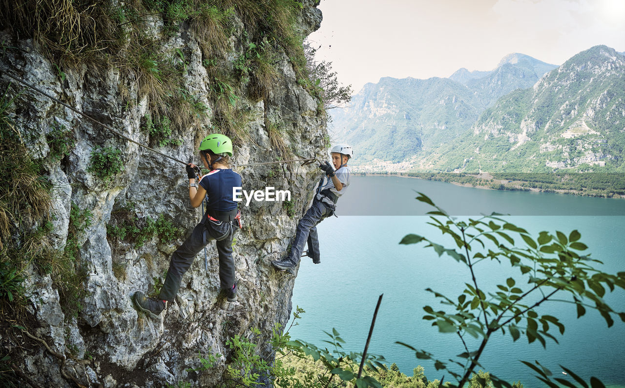 Girl with brother climbing mountain with lake idro in background