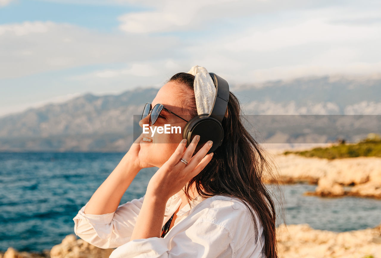 PORTRAIT OF YOUNG WOMAN WEARING SUNGLASSES AT BEACH