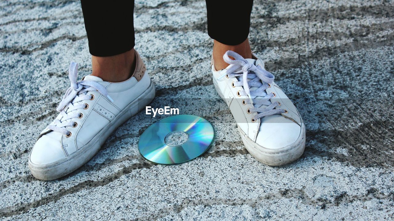 Low section of man standing by compact disc on footpath