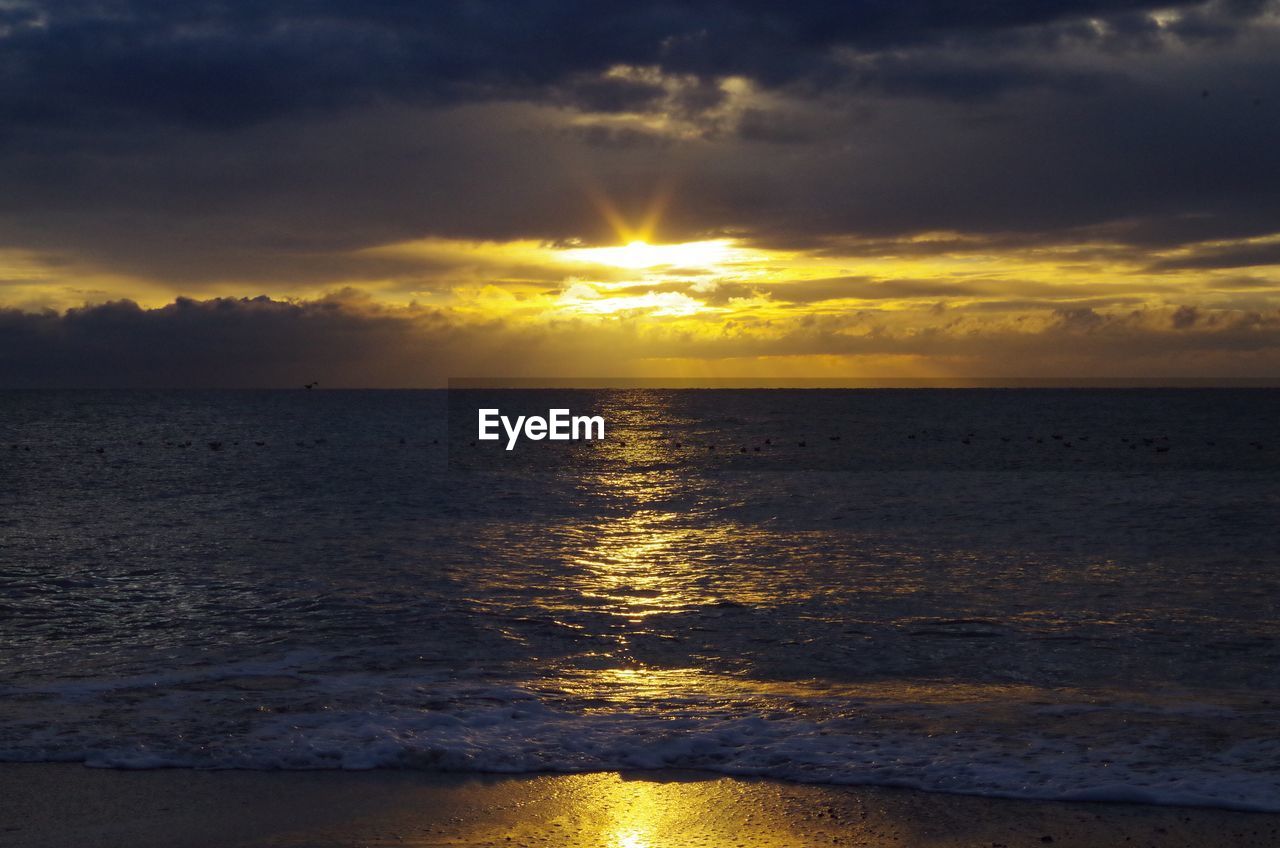 Scenic view of sea against dramatic sky during sunset