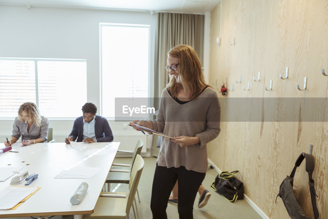 Smiling businesswoman reading document while colleagues working in background at conference table