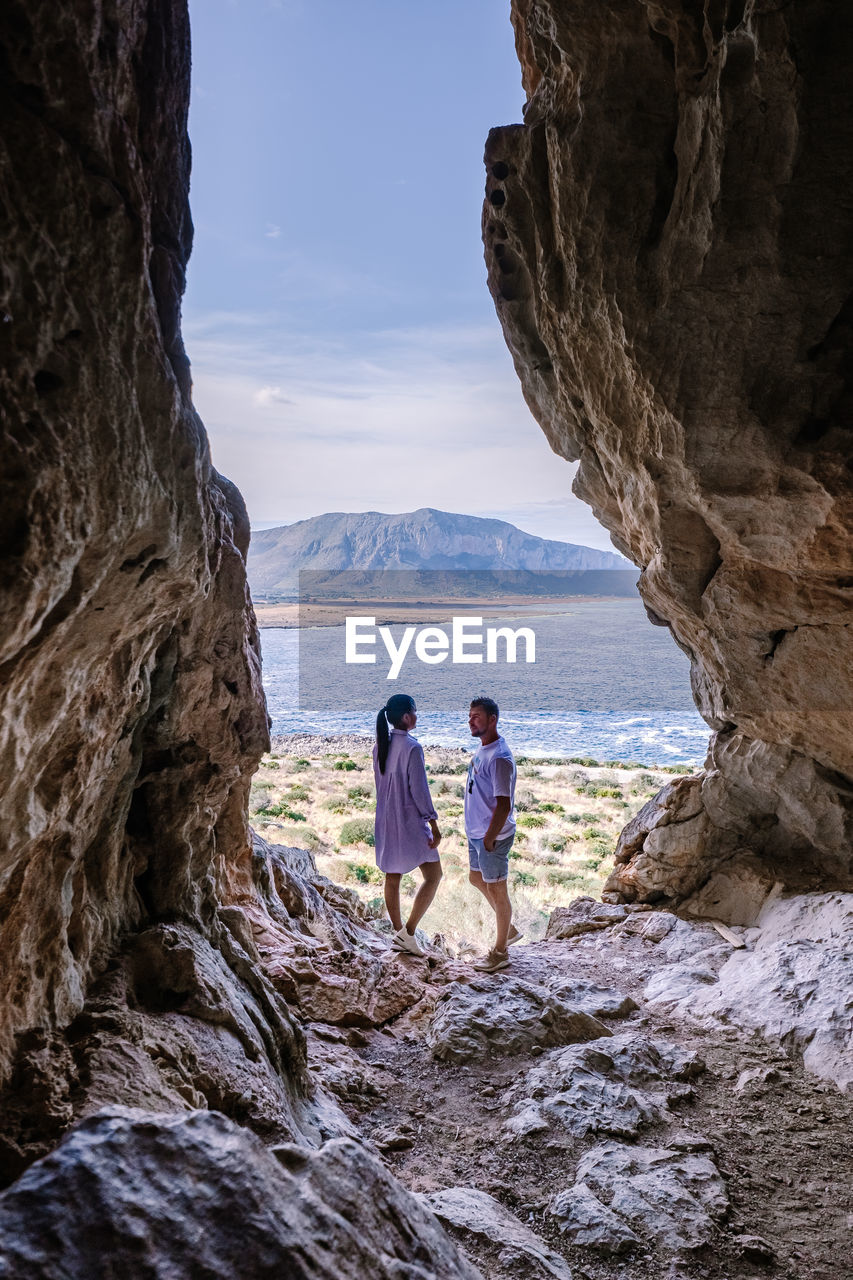 PEOPLE LOOKING AT SEA BY ROCKS