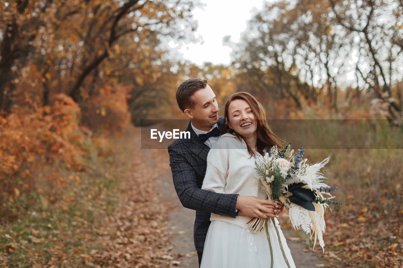 portrait of smiling young woman holding bouquet against trees