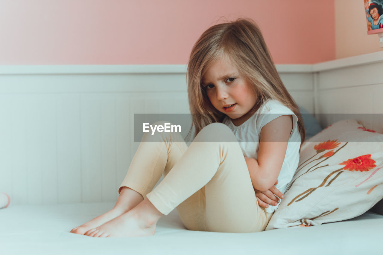 Girl with stomachache sitting on bed at home