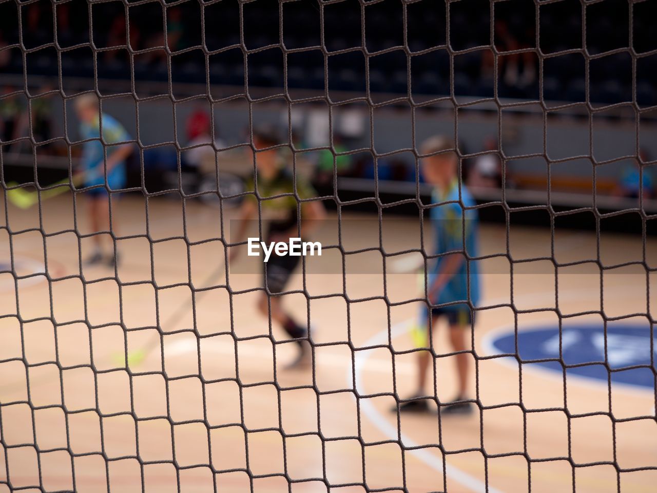 Blurry players of florball. view through protective net of  match. modern surface of florball hall