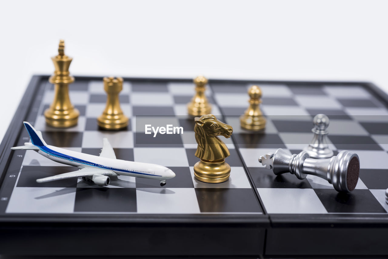 Close-up of model airplane by chess pieces on board against white background